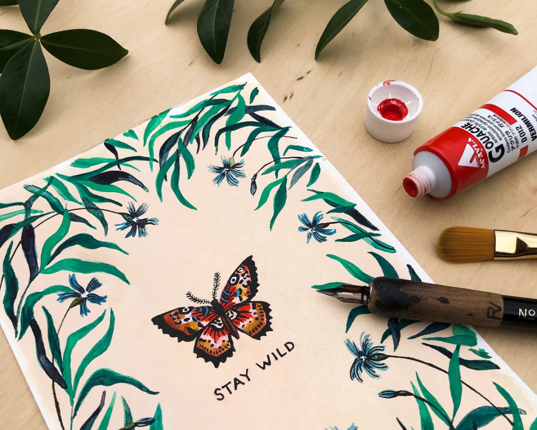 wildship studio watercolor and gouache painting of garden butterfly with green foliage and blue flowers next to a paintbrush and paint tube