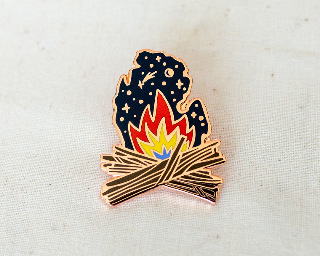 an enamel pin of a campfire and starry night in the shape of michigan