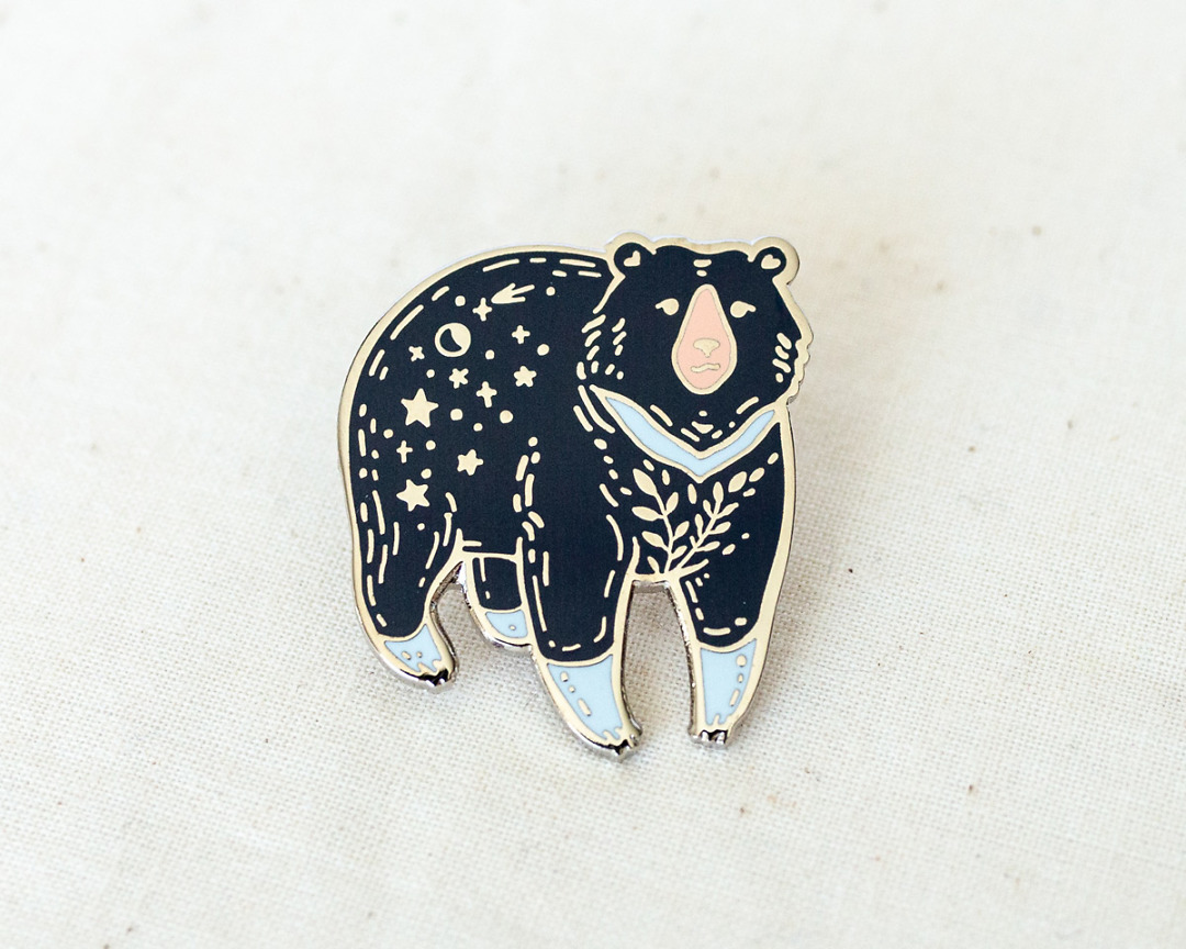 a silvery moon bear enamel pin with stars and moon on its rump