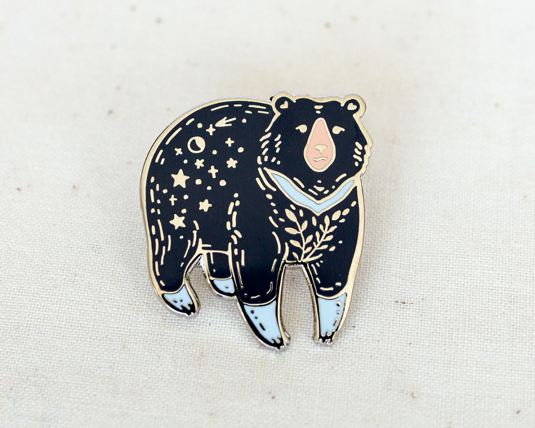 a silvery moon bear enamel pin with stars and moon on its rump