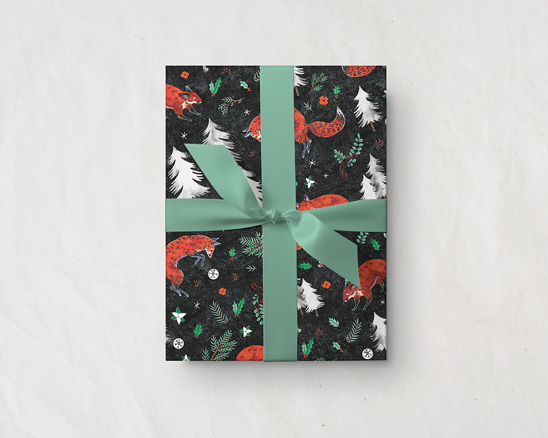 present tied with a green ribbon wrapped up in Wildship Studio holiday gift wrapping paper with fox, pine trees, snowflakes, poinsettia, and holly